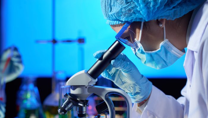 Profile view of concentrated Asian microbiologist examining sample with help of modern microscope while wrapped up in work at dim laboratory