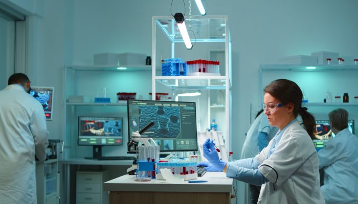 Medical lab worker analyzing blood serum conducting virus test in modern equipped lab late at night. Team of specialists examining vaccine evolution using high tech for treatment against covid19